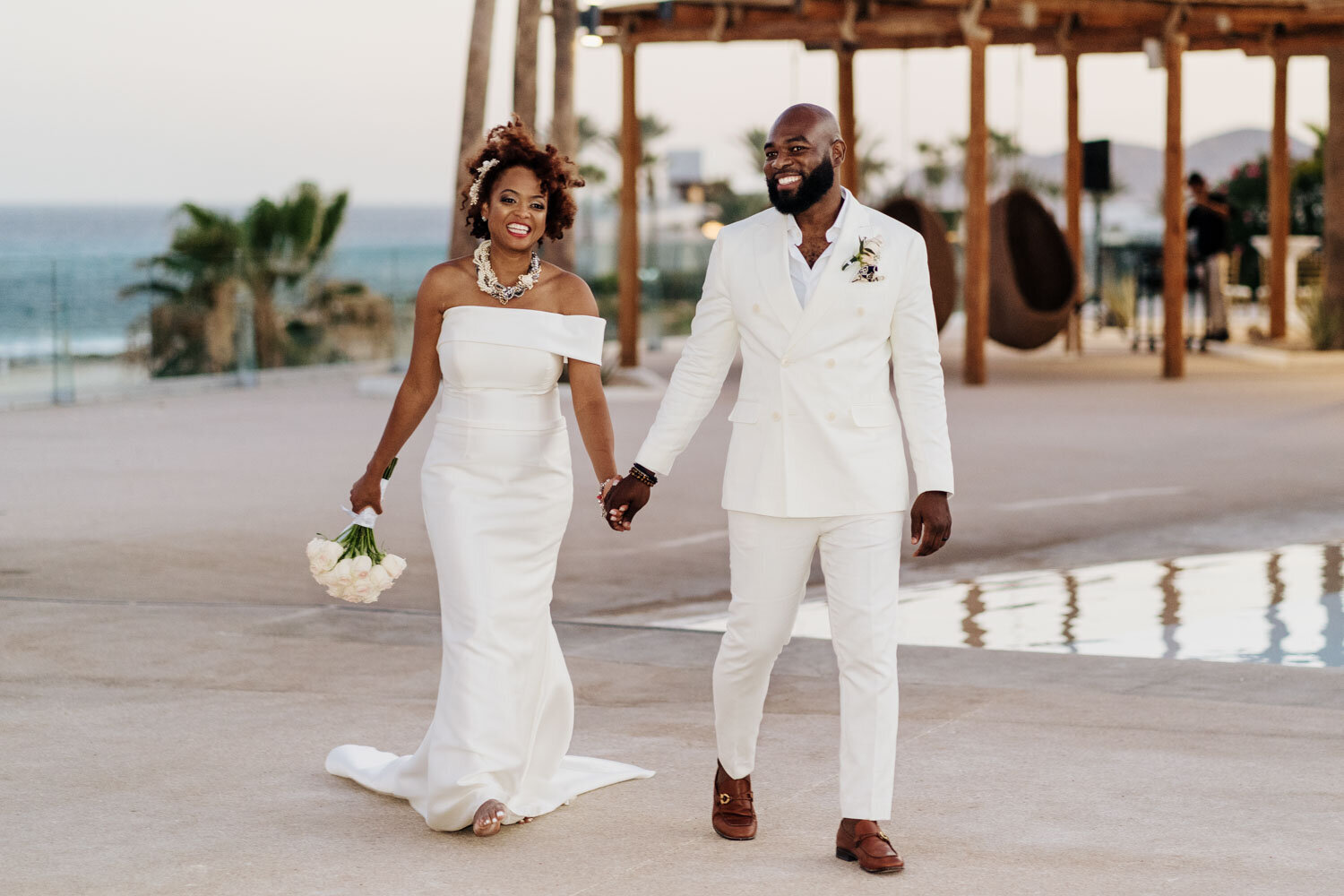 Bride and groom walking joyfully by a poolside venue