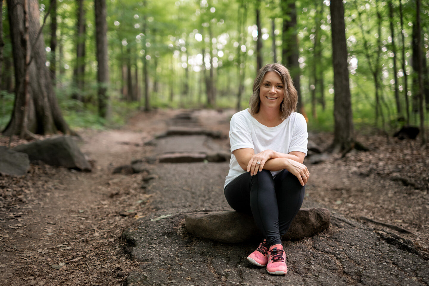 Jen heller sitting on a large rock in the woods