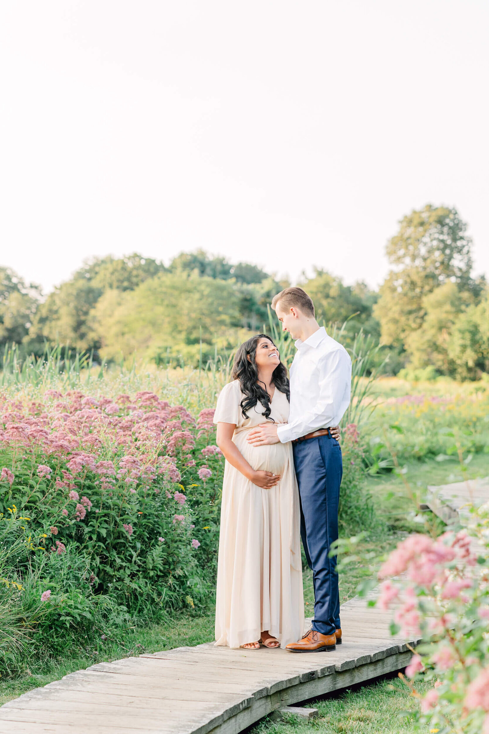 Woman holding her baby bump looks up at her husband, whose hand is on the top of her belly