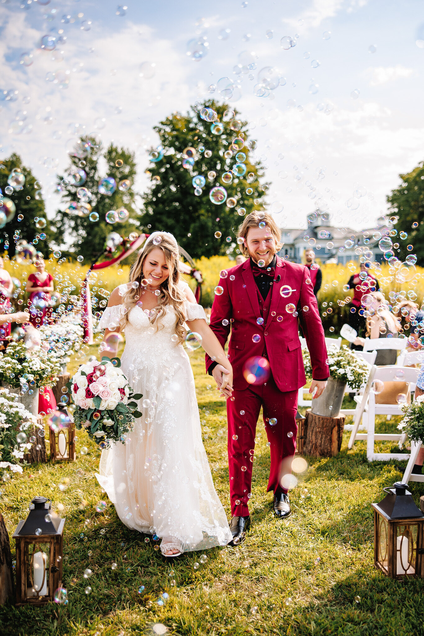 A bride and groom proceed down the isle of their outside ceremony, surrounded by bubbles blown by their guests