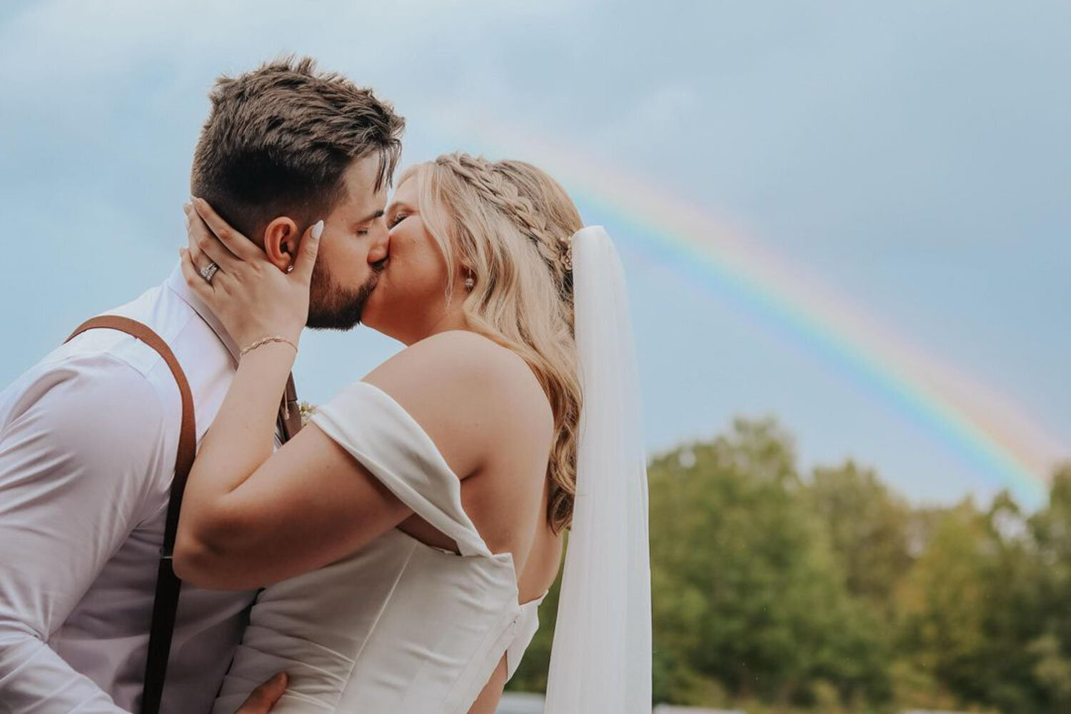 Bride and groom kissing with a rainbow view