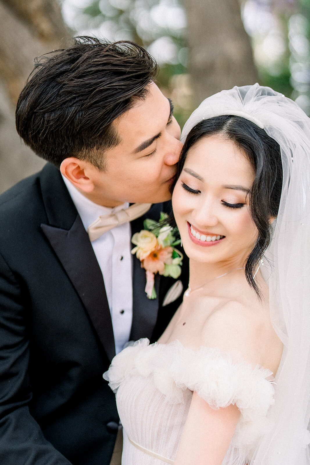 The groom lovingly kisses the bride’s cheek, capturing a tender and intimate moment on their wedding day at Stanford University.