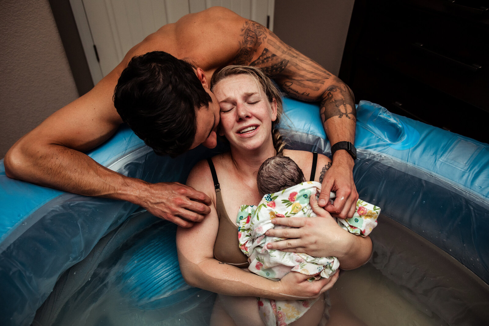 dad holding mom as she emotionally holds her new baby girl in the birth tub