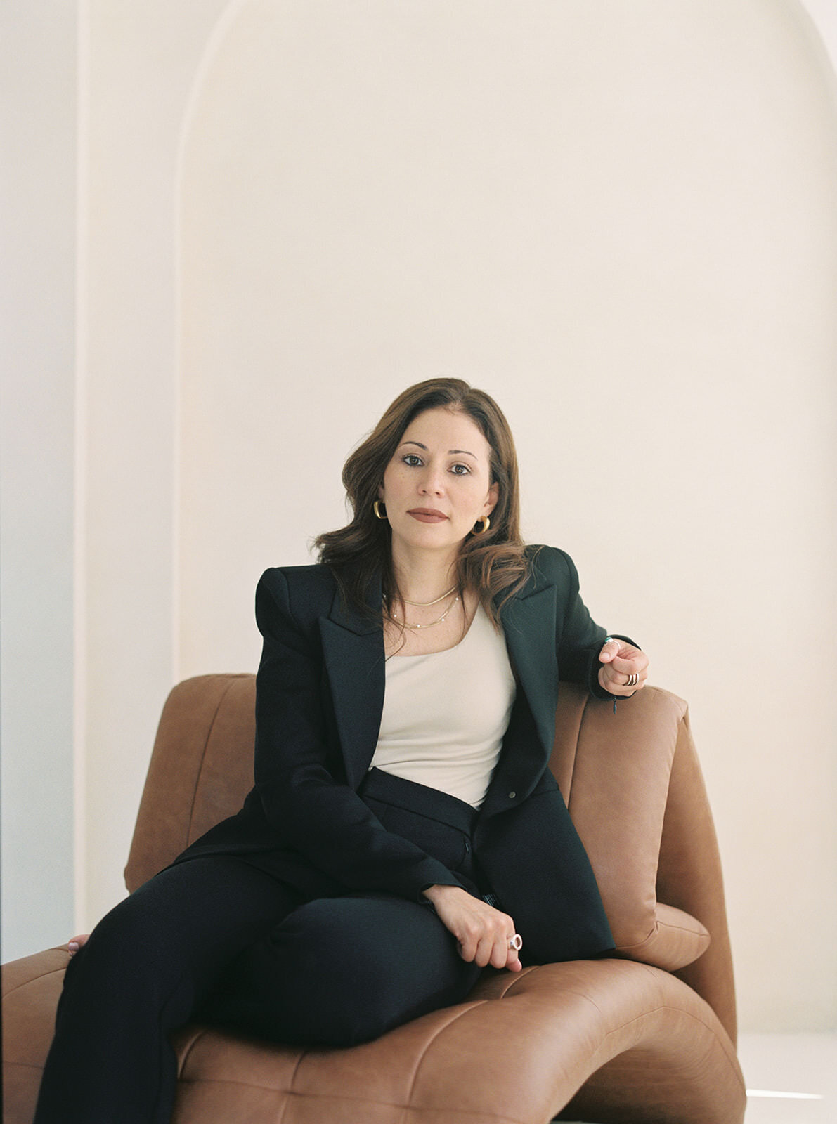 Modern branding portrait of a woman leaning on a stylish leather chair, highlighting her poised demeanor.