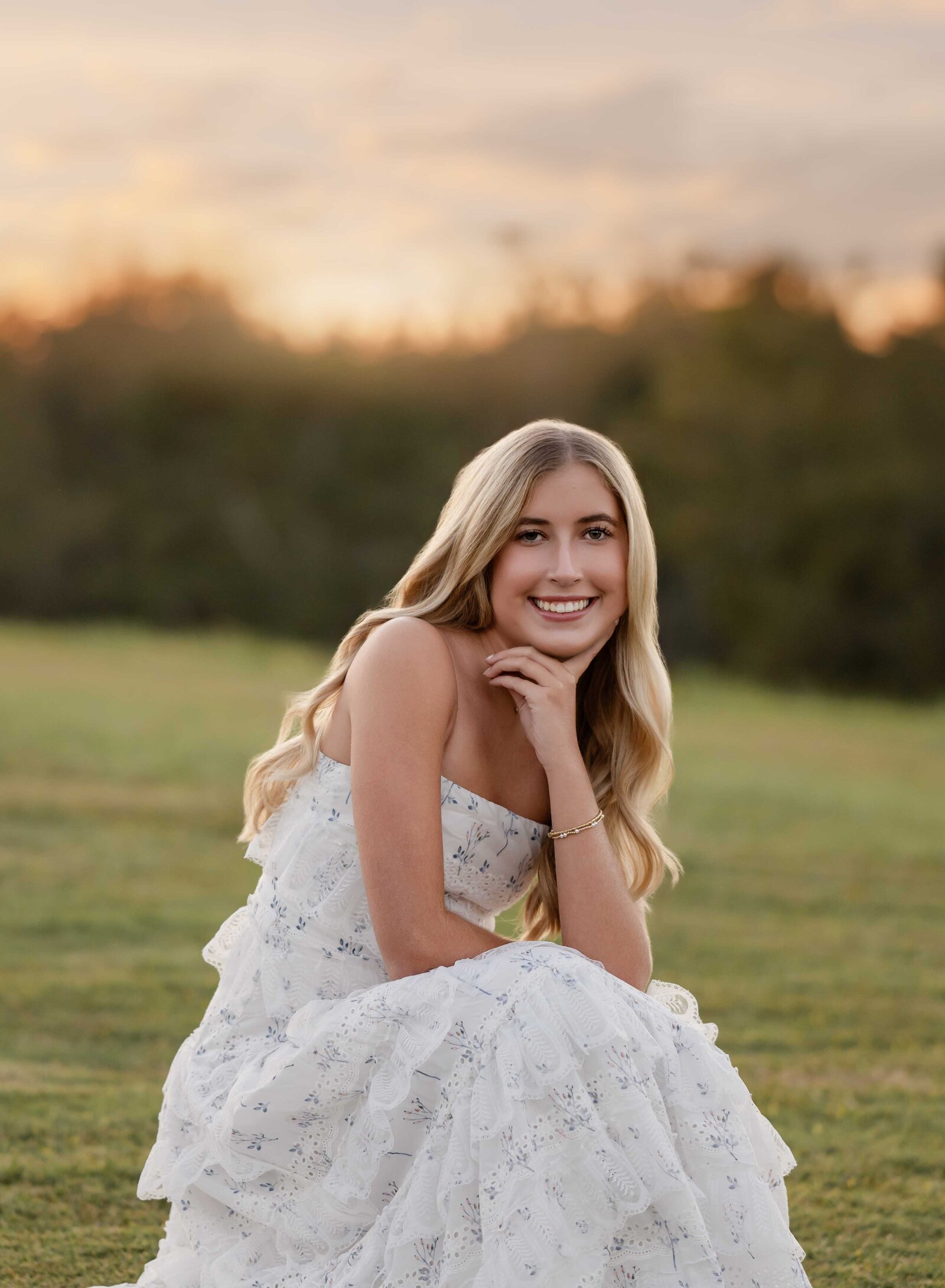 Girl kneeling down in open field and smiling while taking a Senior photo. Senior graduation photos taken by Jenni Nikki Photography in Atlanta, GA