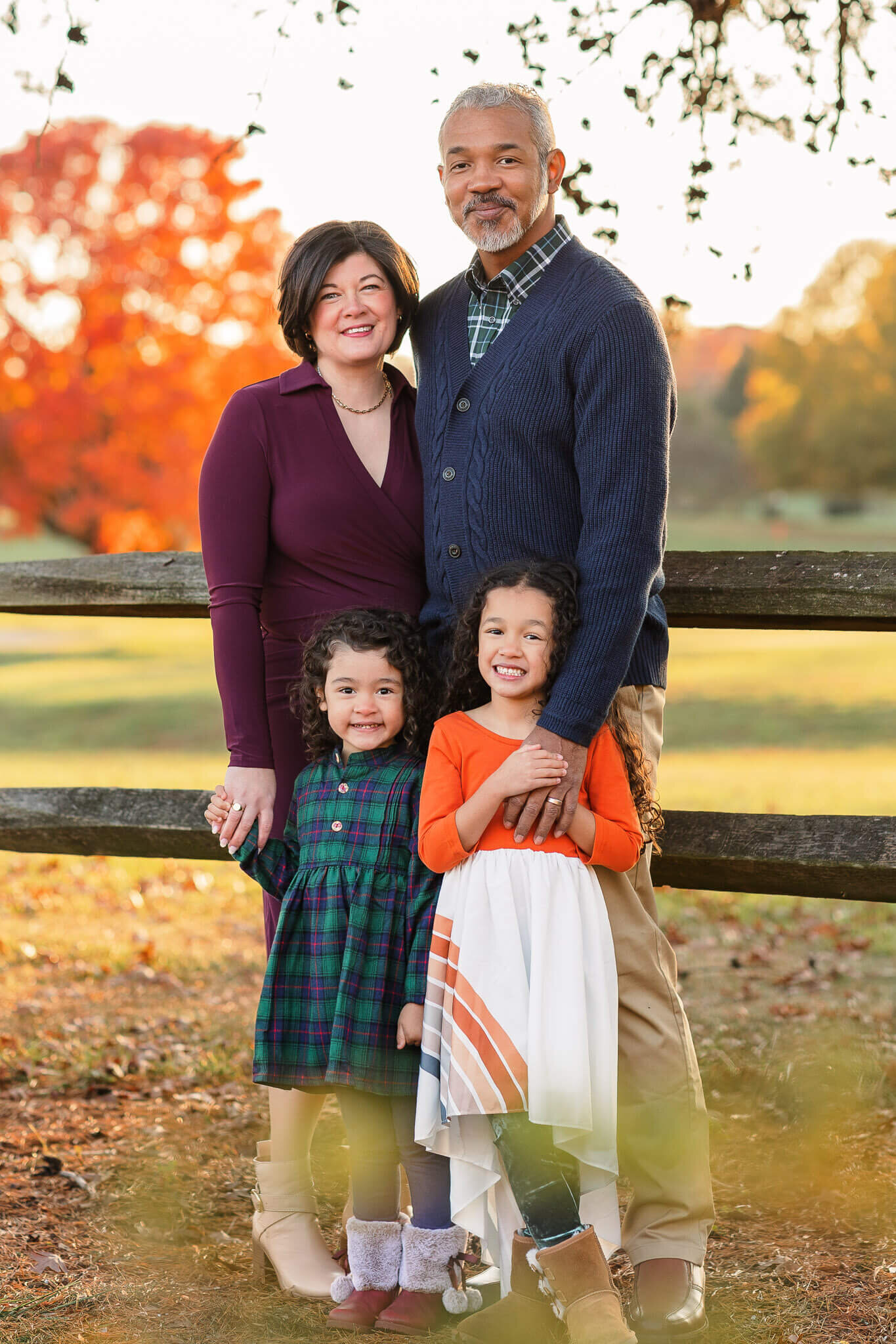 A family of four standing against a fence with orange trees in the background