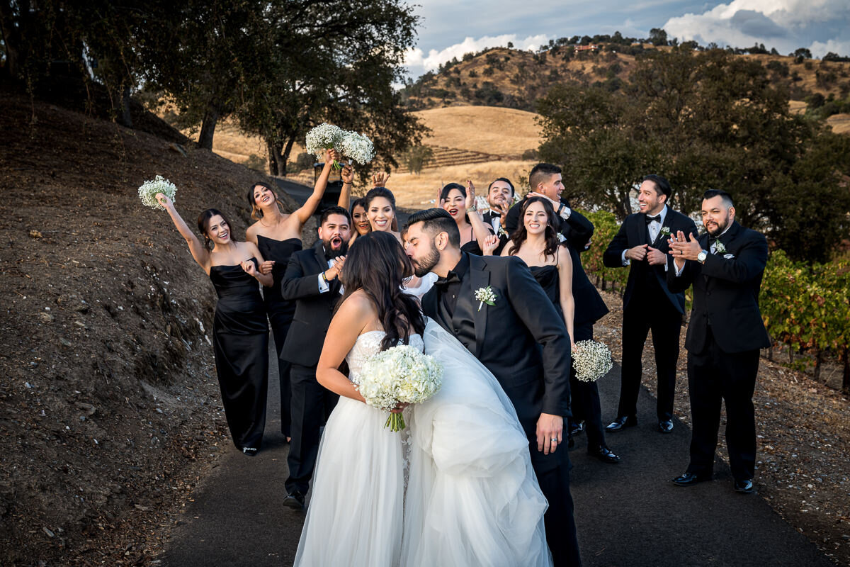 A joyful moment with the bridal party celebrating against the backdrop of sprawling vineyards and a vibrant California sky.