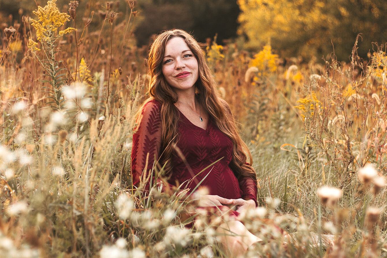 Pregnant women sitting in blooming meadow. Looking straight into the camera , smiling, radiantly glowing. Maternity Photography.