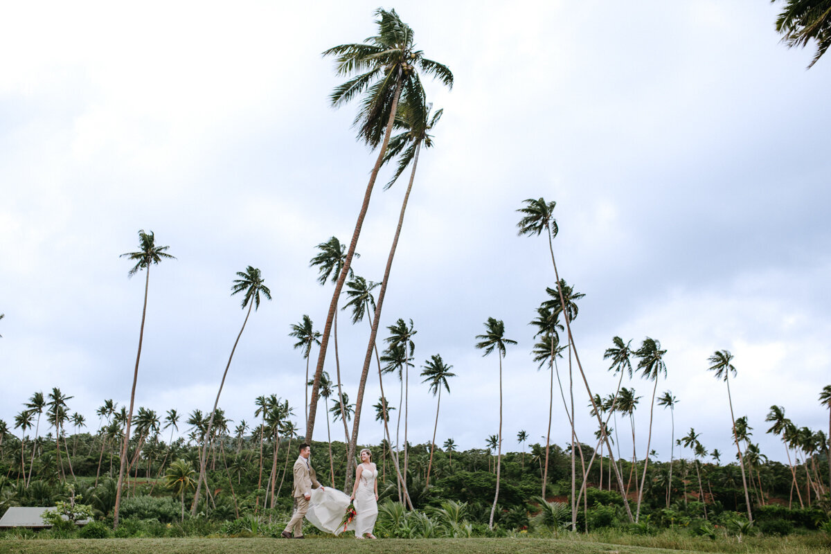 bride and groom walking under palm trees