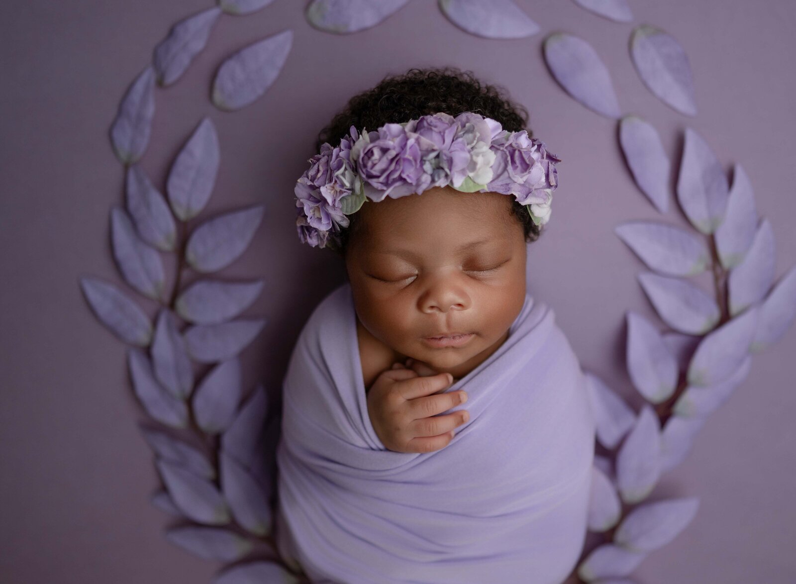 Baby in purple swaddled, sleeping, and surrounded by purple leaves. Photographed by Atanta newborn photographer.