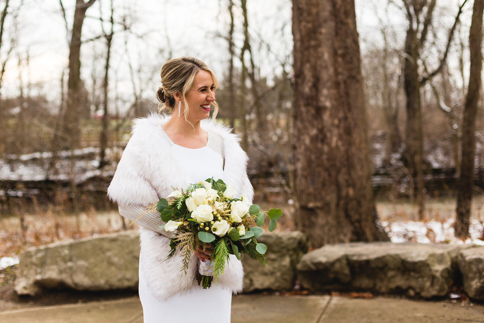 bride looking at her groom and smiling while wearing fur and holding flowers at winter wedding ohio