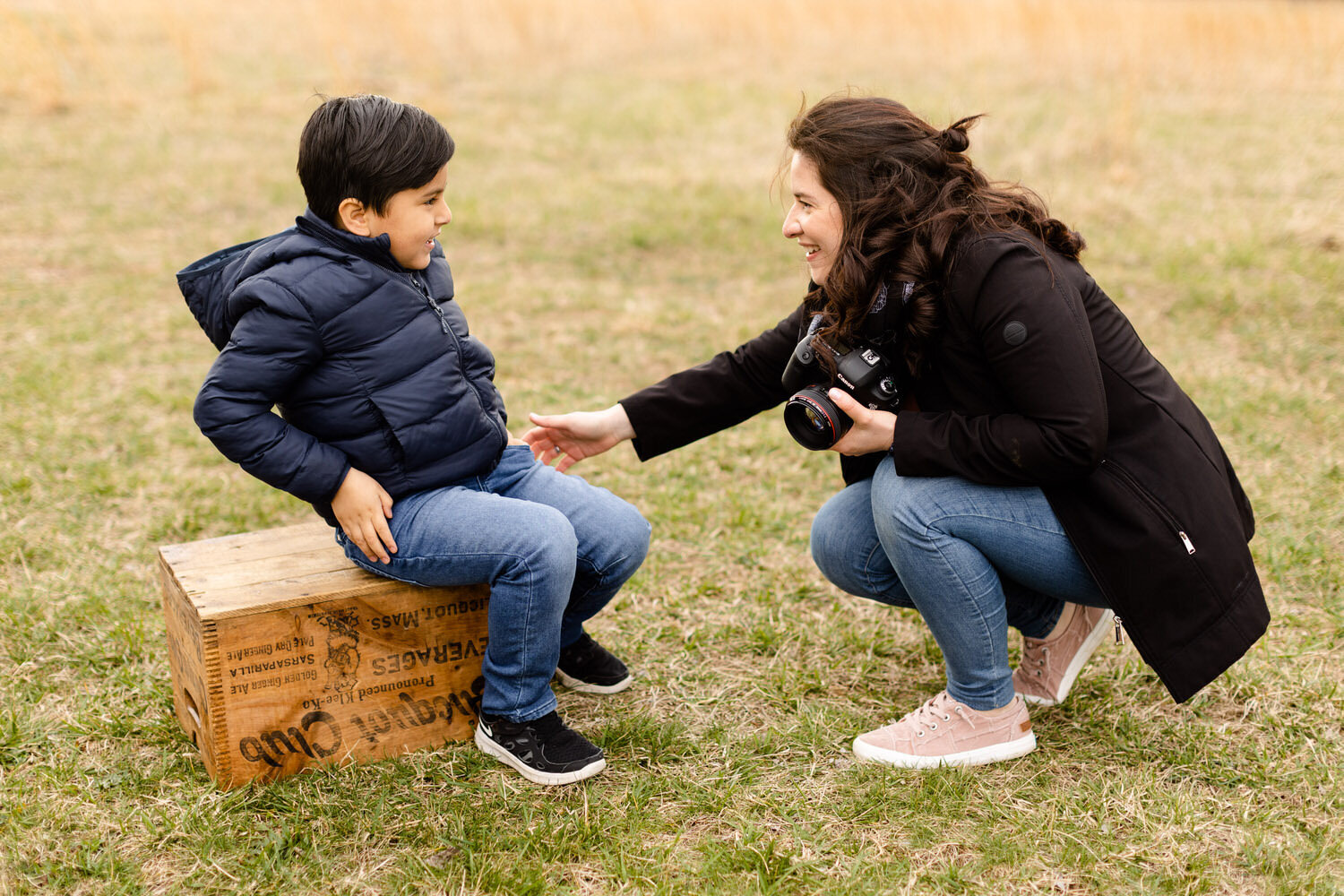 photographer bent down talking to young child who is sitting on a wooden box