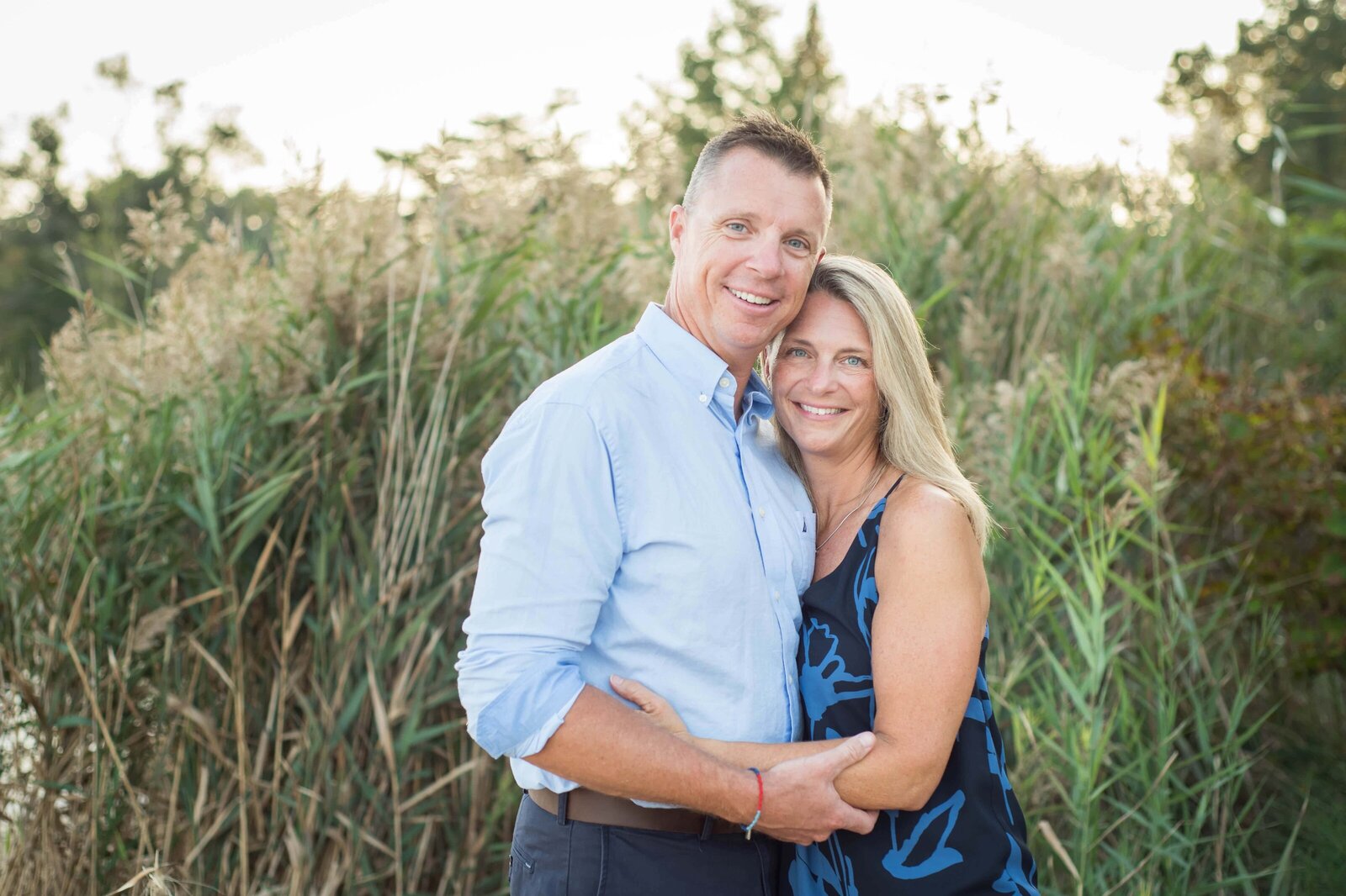 Couple hugging in their family portrait with tall grasses behind them