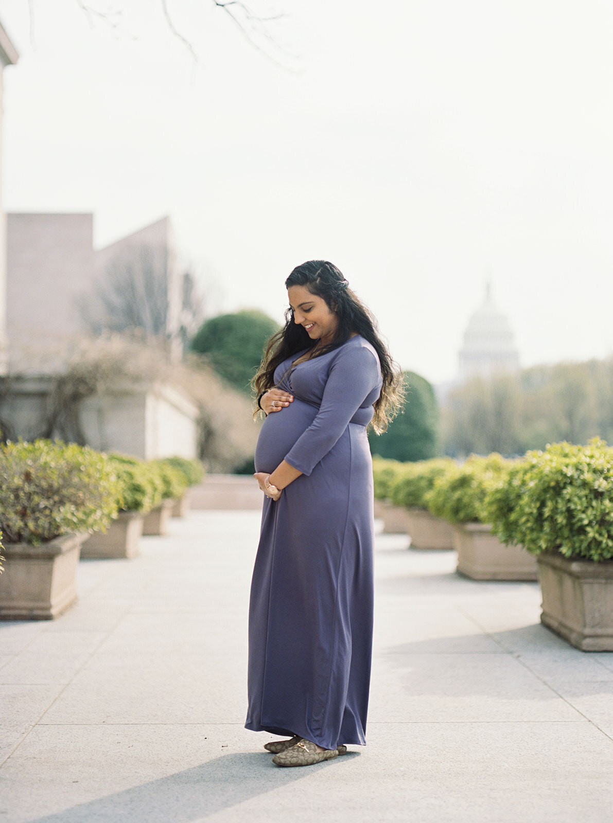 Radiant expectant mother in a long purple dress, cradling her belly with the U.S. Capitol in the background.