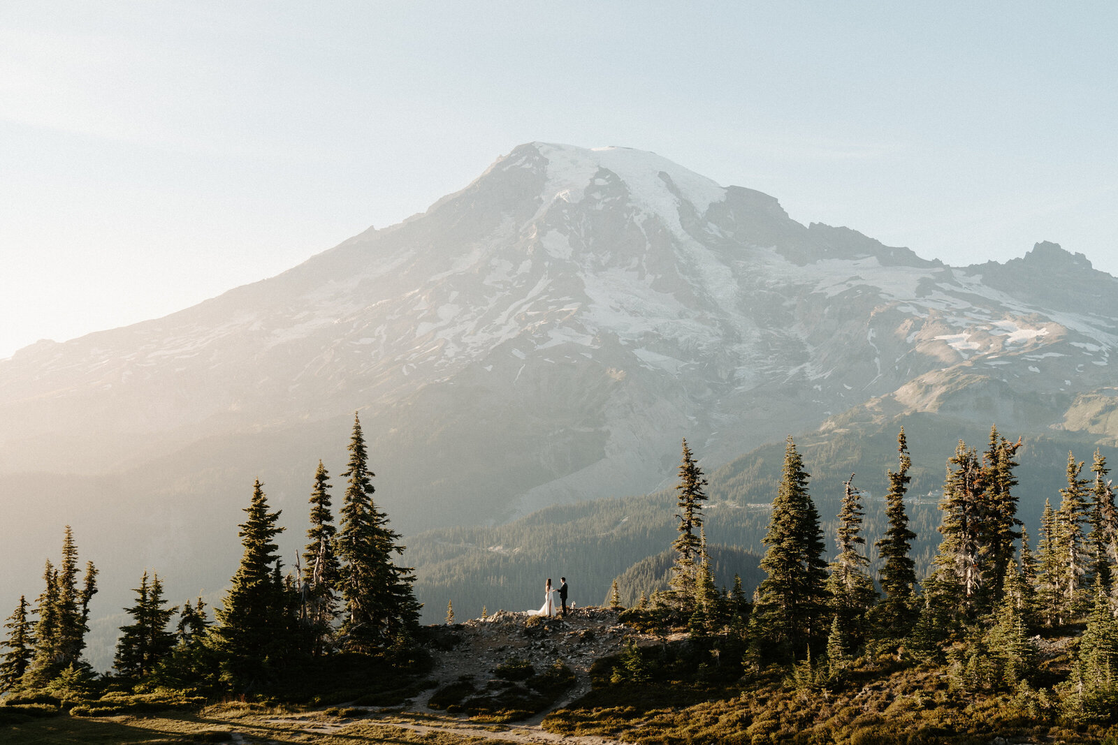 Bride and groom kissing for a wedding portrait in front of Mount Rainier with the bride's veil flowing behind her