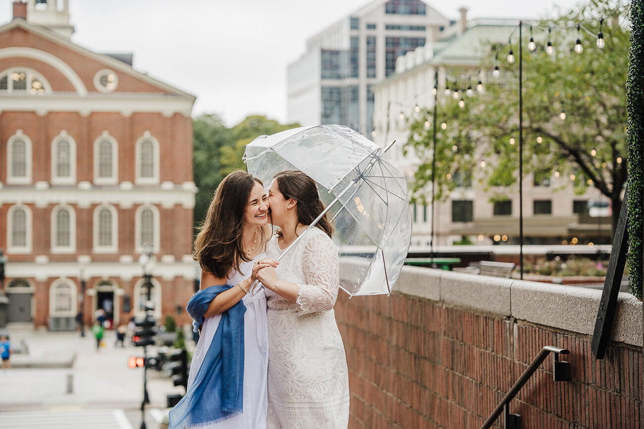 two brides kiss under an umbrella after boston city hall elopement