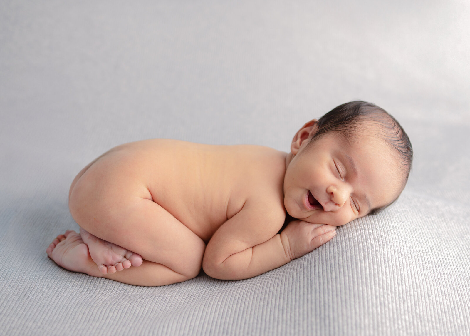 Newborn baby sleeping on a light gray blanket with a peaceful smile during an in-studio newborn session in Bergen County, NJ