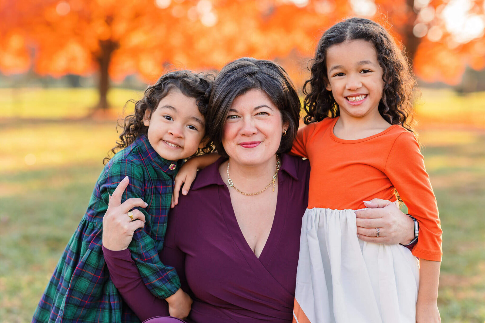 A mom with her two daughters at a park in the fall at sunset.