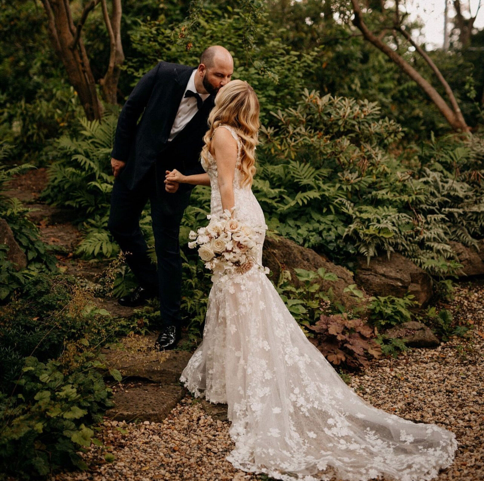 bride and groom kissing in a lush, green garden