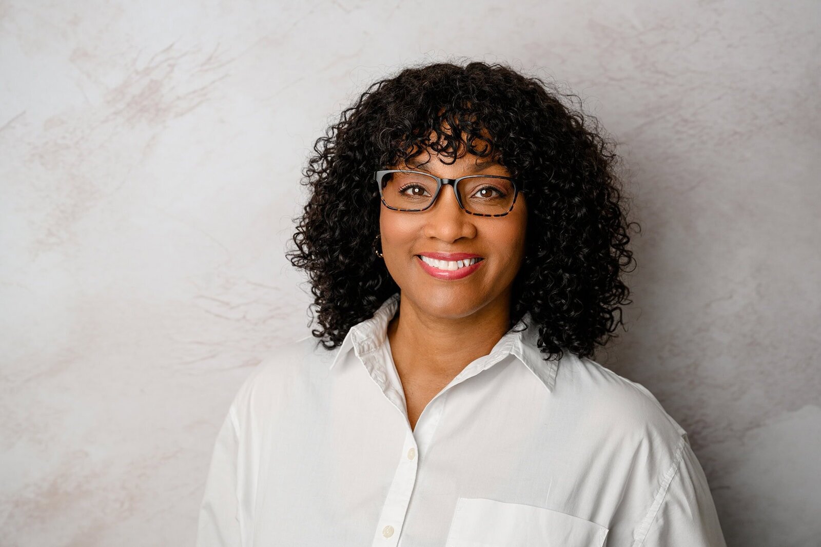 Charlotte woman wearing white button down and glasses with cream background