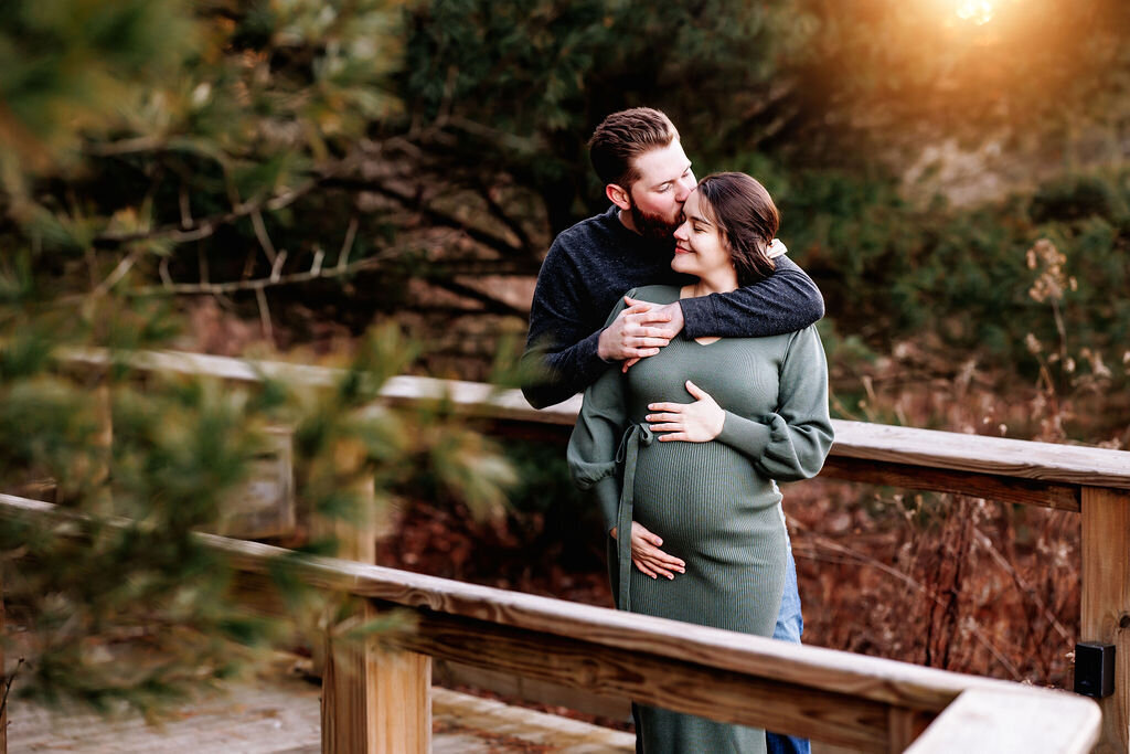 Man snuggles up with his pregnant wife along a wooden walkway