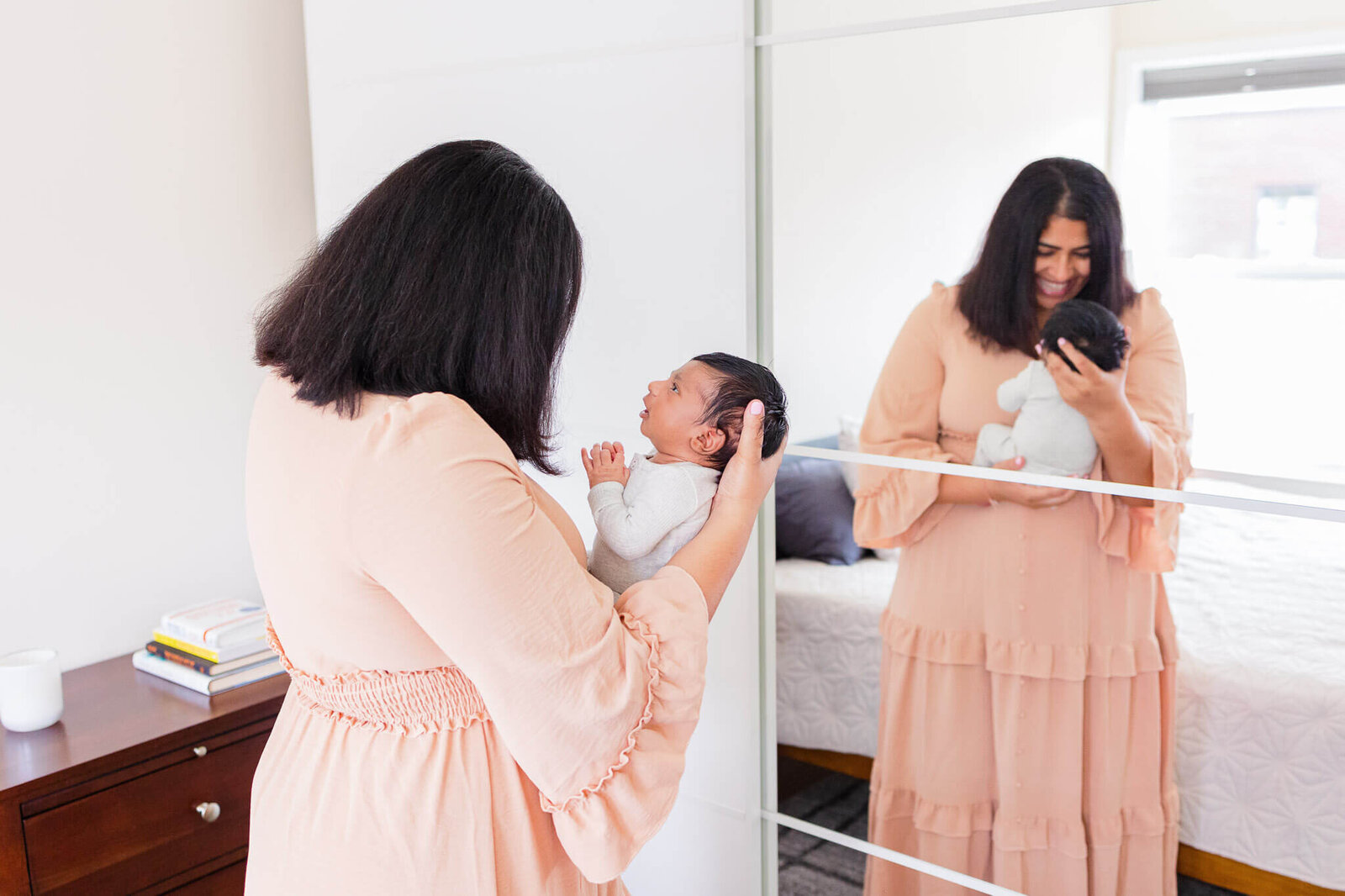 A mom holding her newborn son and smiling at him with a reflection of them in the mirror.