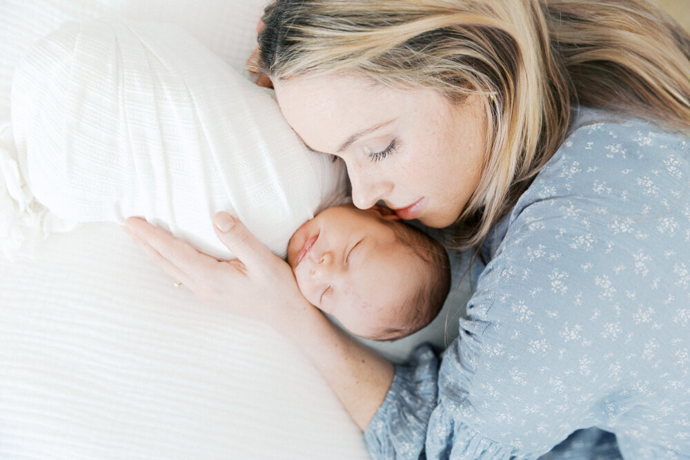 Image of mother in blue dress laying next to newborn baby aken by Newborn Photographer Sacramento Kelsey Krall Photography