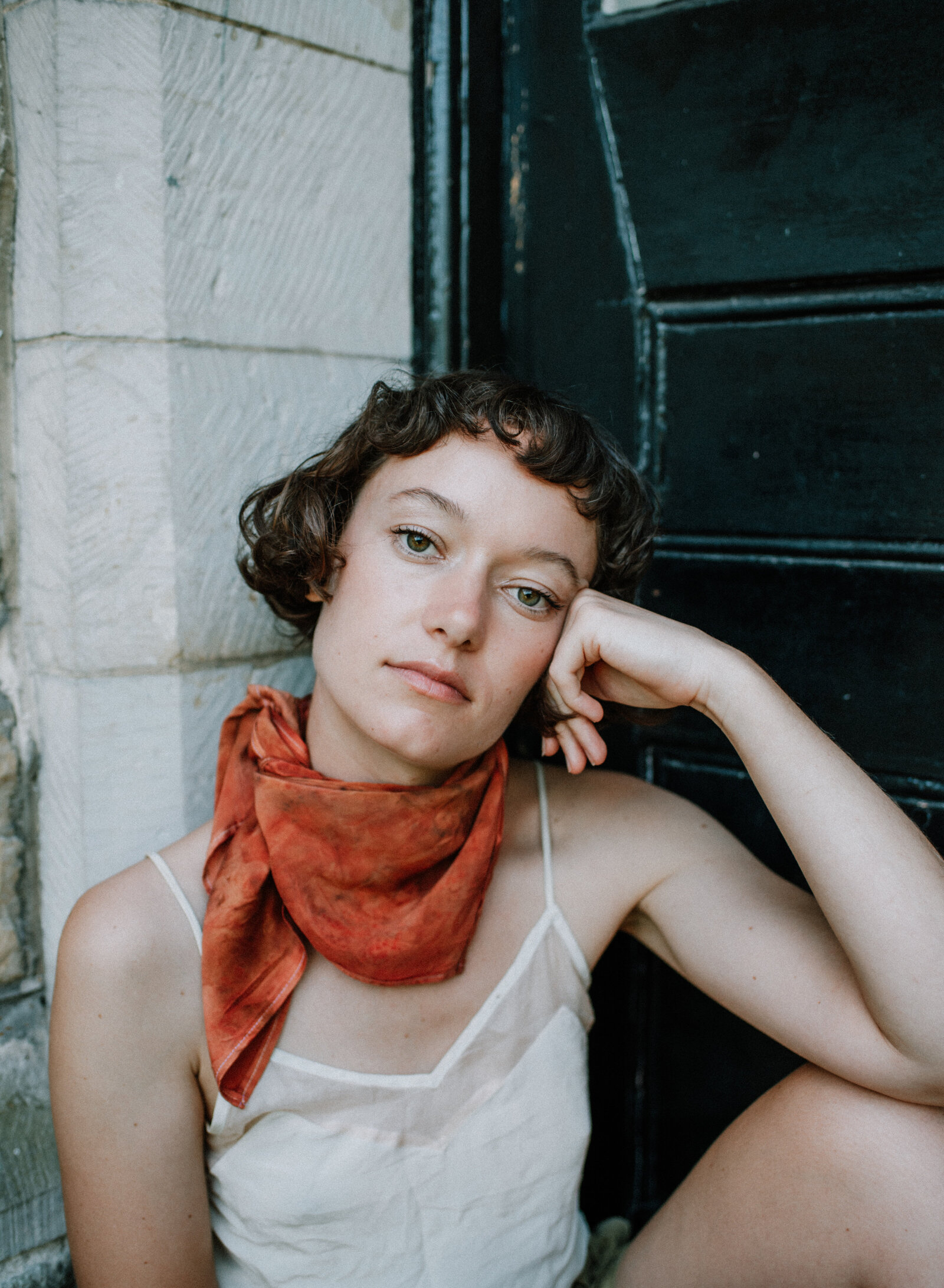 curly haired woman is wearing a red dyed silk scarf, looking confidently at the camera