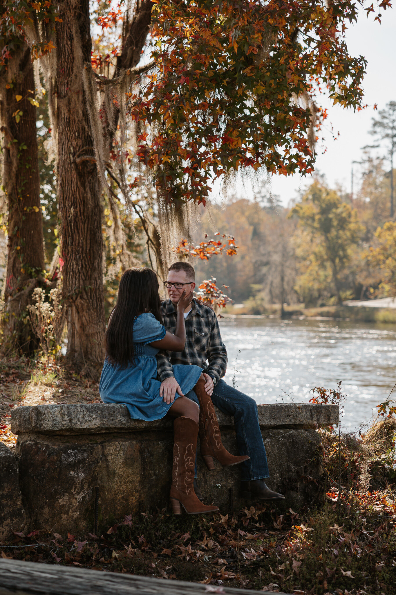 Couple sitting together beside the river during a fall couples session at Savannah Rapids in Evans GA.