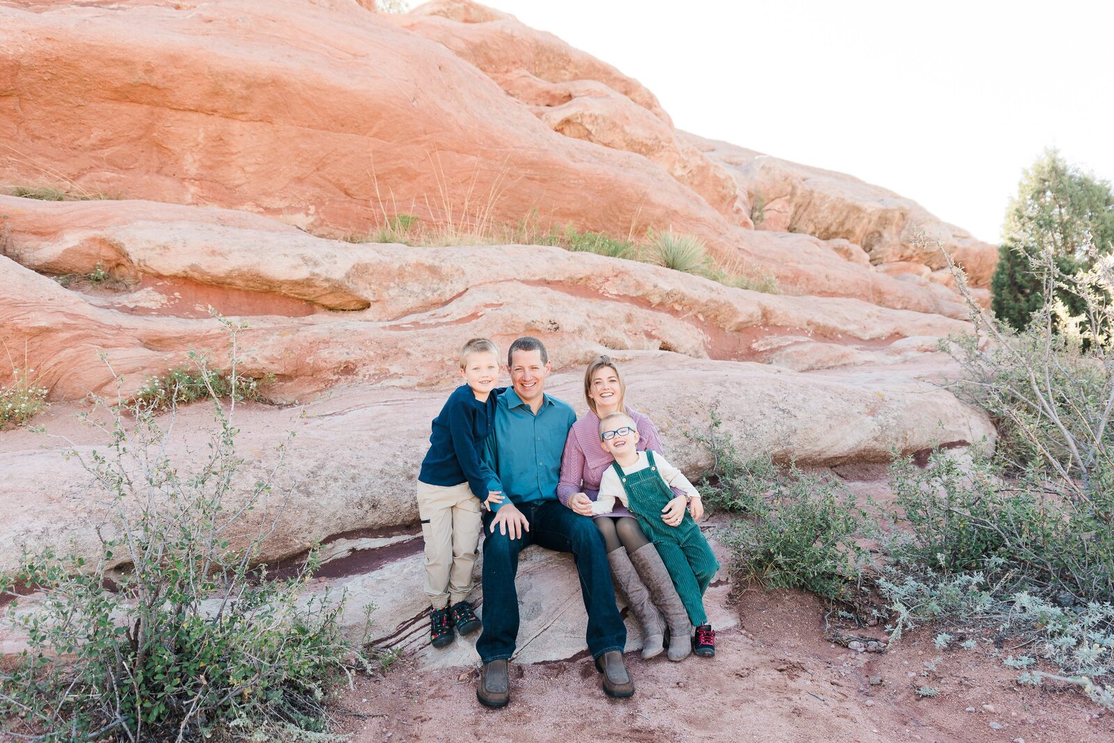 A family sits on the edge of some rocks in front of Red rocks captured by denver family photographer