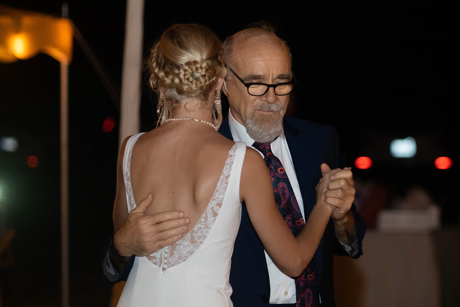 bride with low cut back dress and braided updo hairstyle hugging father in black tux with glasses during father daughter dance at wedding reception by wedding photographer in nashville klem photography