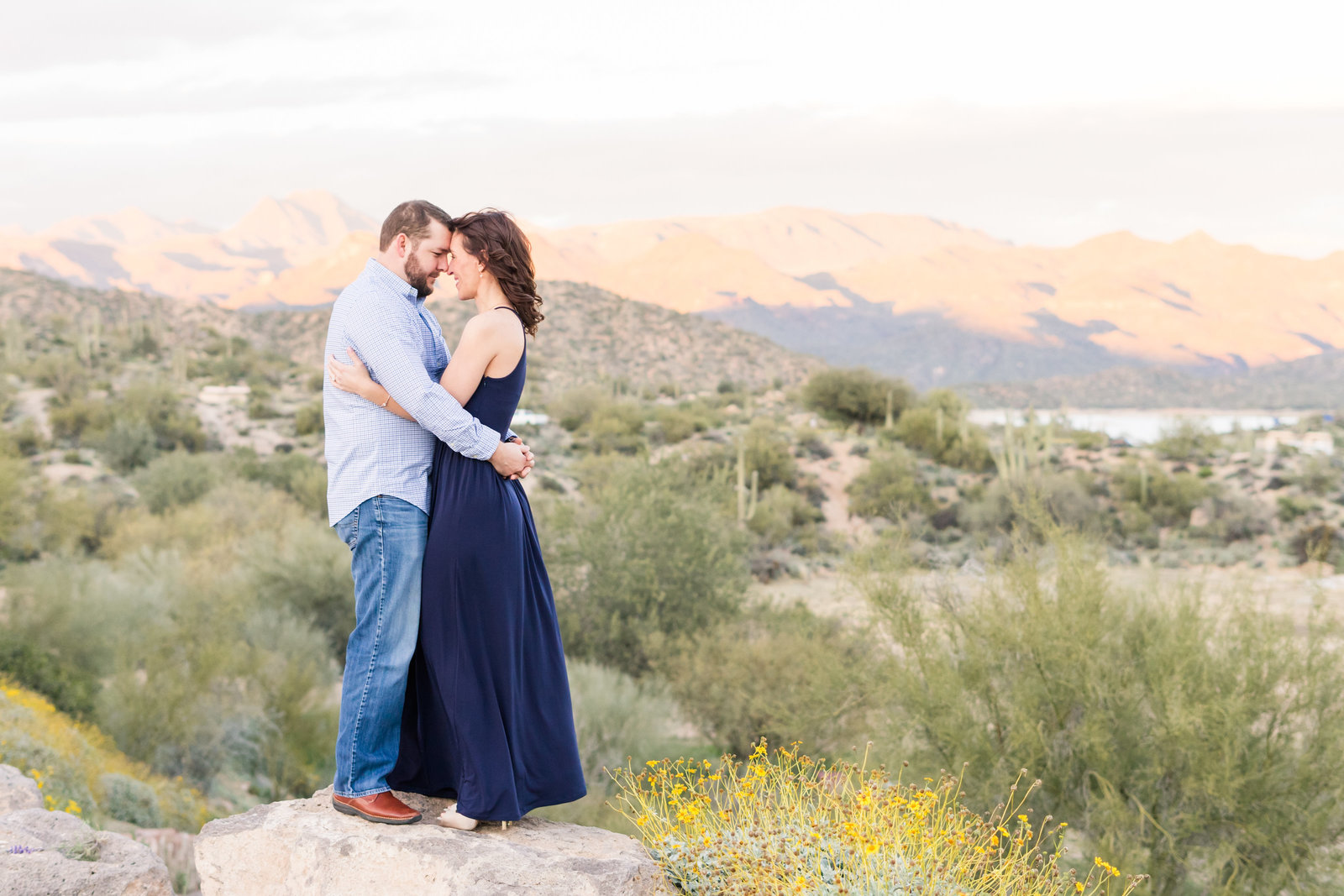 Couple cuddling on top of rock in front of mountains in desert