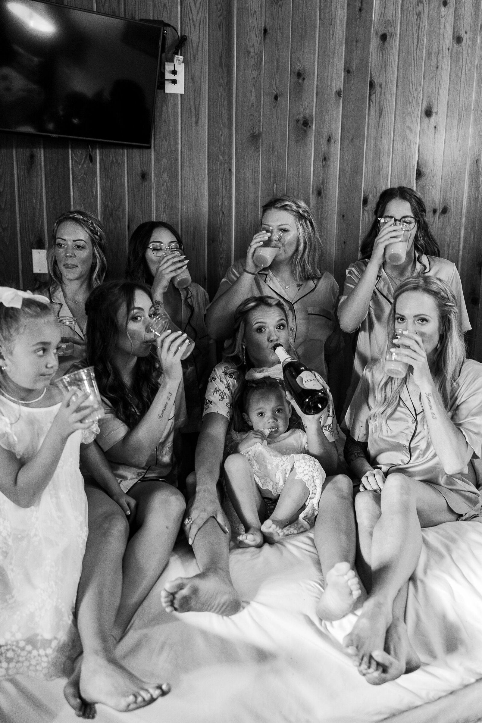 Bridesmaids all together on bed holding champagne glasses before wedding 