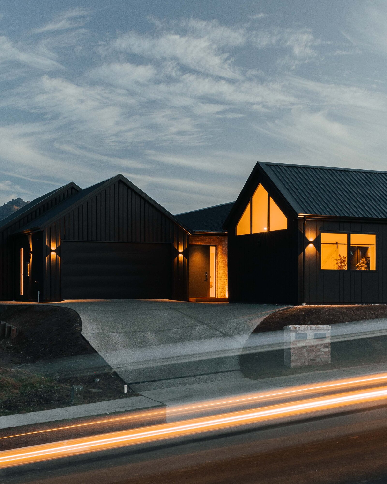 A night view of the exterior of a home featuring timber cladding, brick features and James Hardie Oblique cladding on a home built by Twin Peaks Construction in Hanleys Farm, Queenstown.