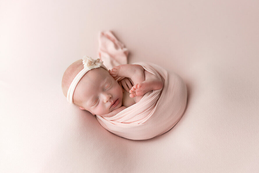 Newborn baby sleeps on a pink backdrop for her photo session at Angela Marie Media.