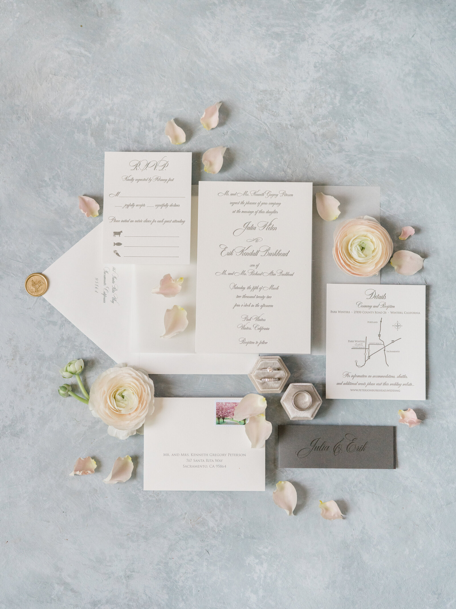 wedding invitations and wedding rings against a light blue background