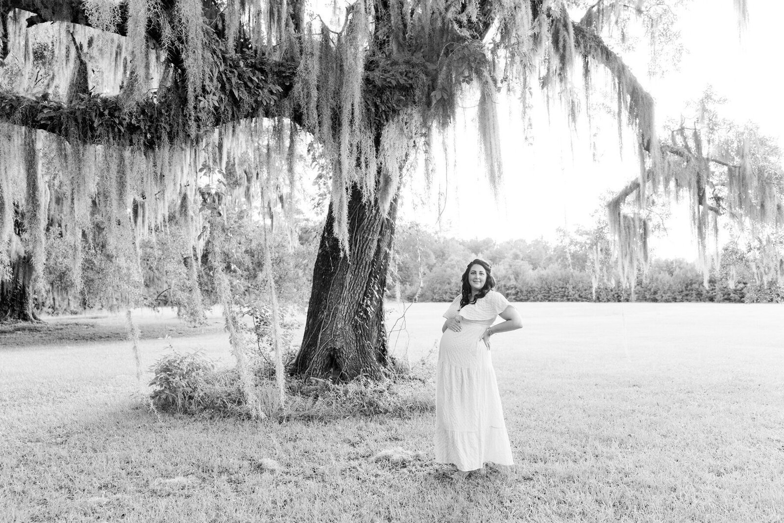 Expectant mother standing under an oak tree with Spanish moss to show maternity photography savannah