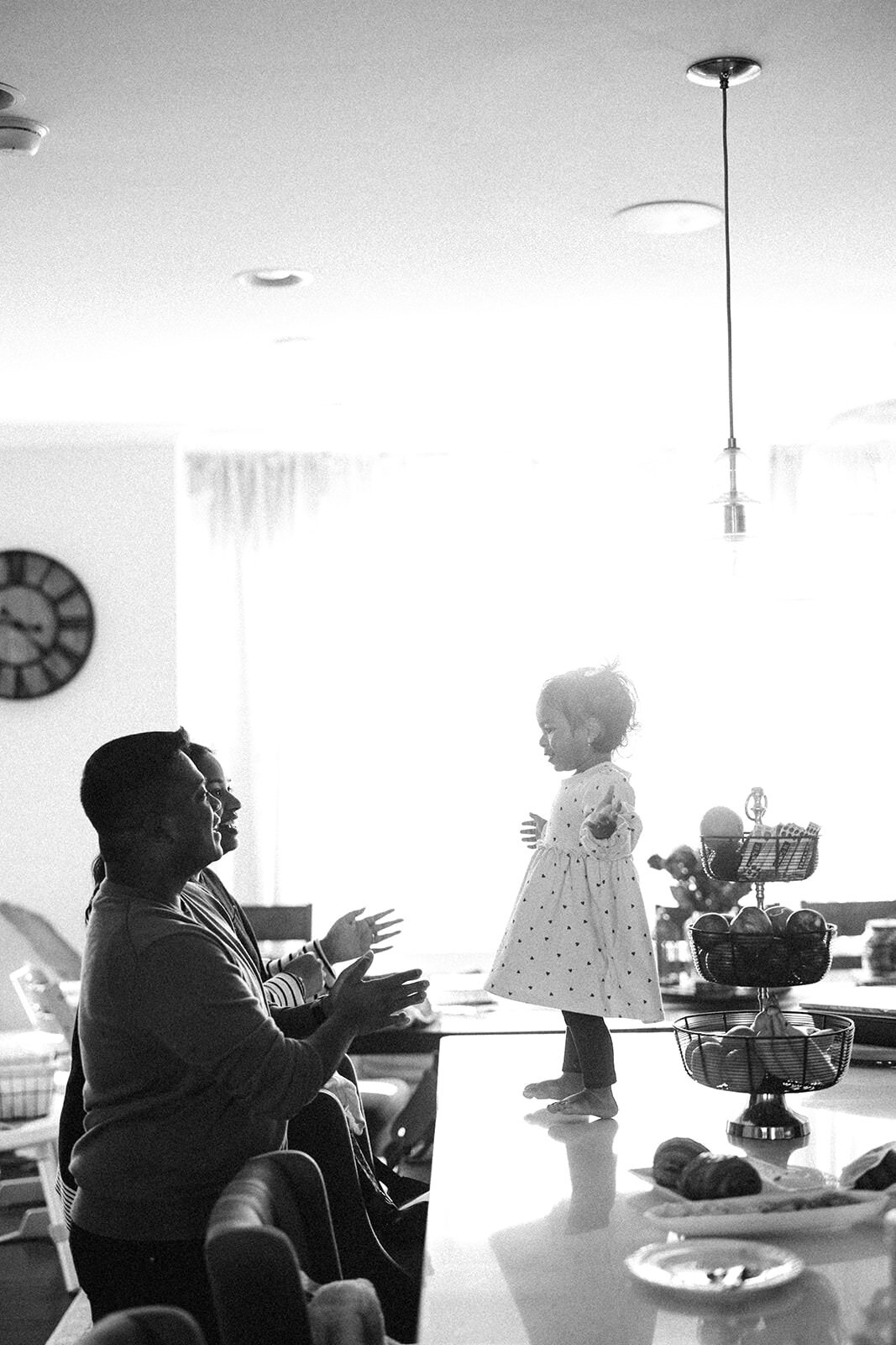 Family laughing and interacting with their toddler standing on a kitchen counter.