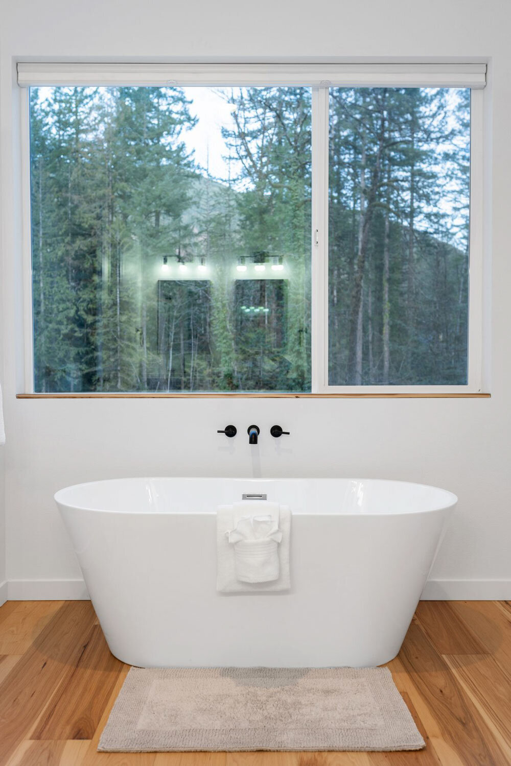 White freestanding bathtub in front of a large window with forest view