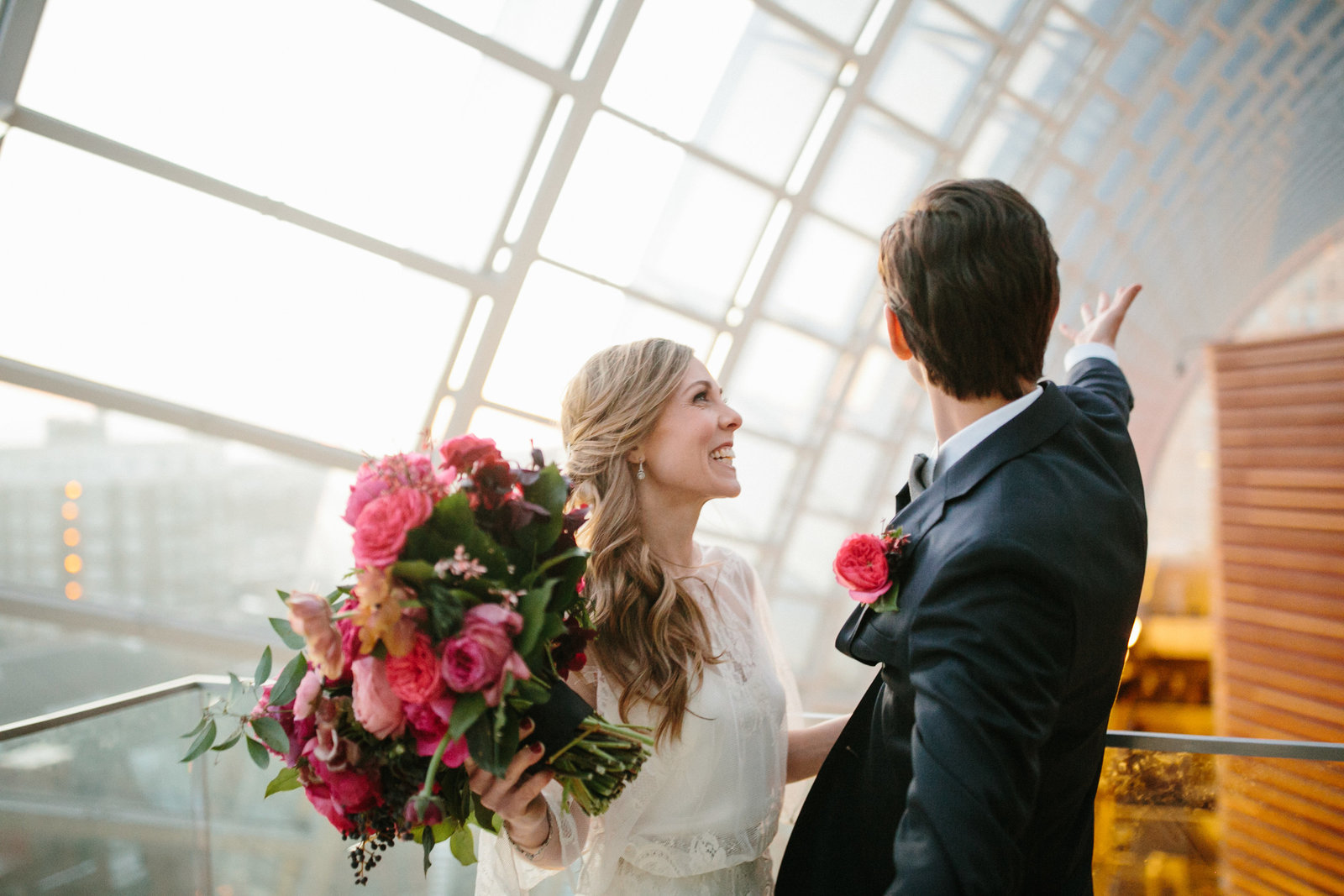 Bride and groom photographed at this iconic spot at the Kimmel Center with soft natural light pouring in, and a big pink floral bouquet by Wild Stemes.