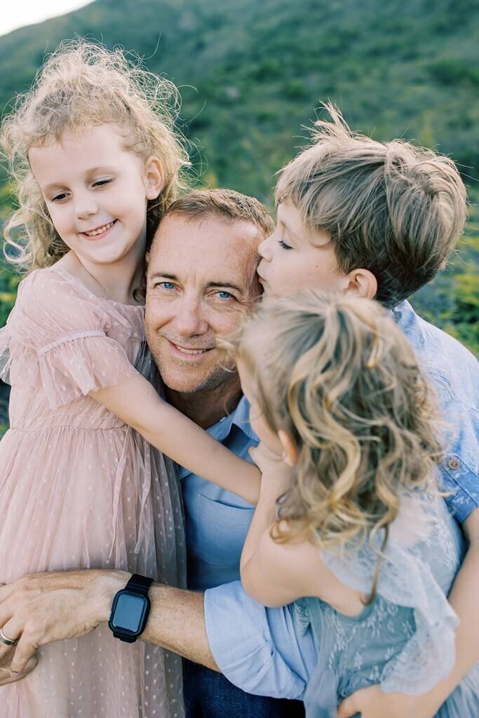 Father hugging his three children while one of them gives him a kiss.