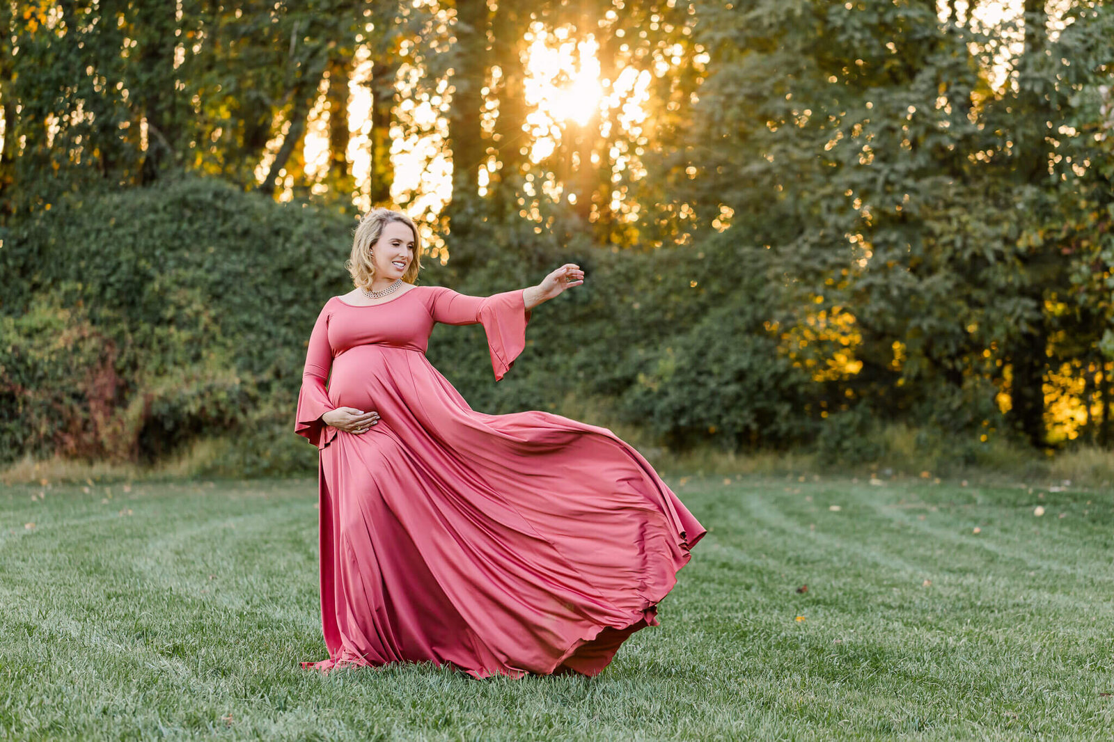 A beautiful mother-to-be tossing her pink dress at a park in Fairfax at sunset.