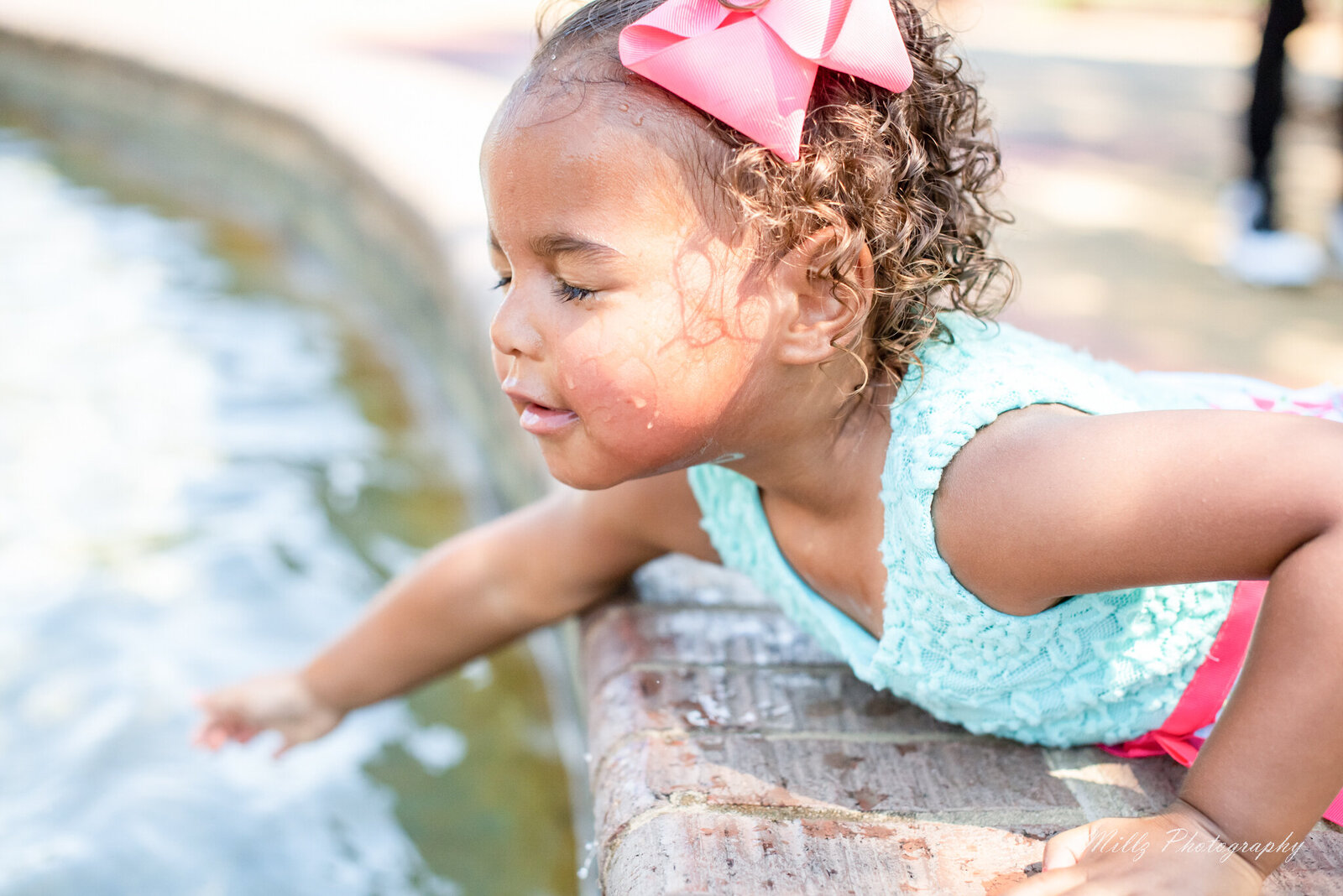 young girl standing over a fountain dipping her hands in the water with her eyes closed photographed by Millz Photography in Greenville, SC