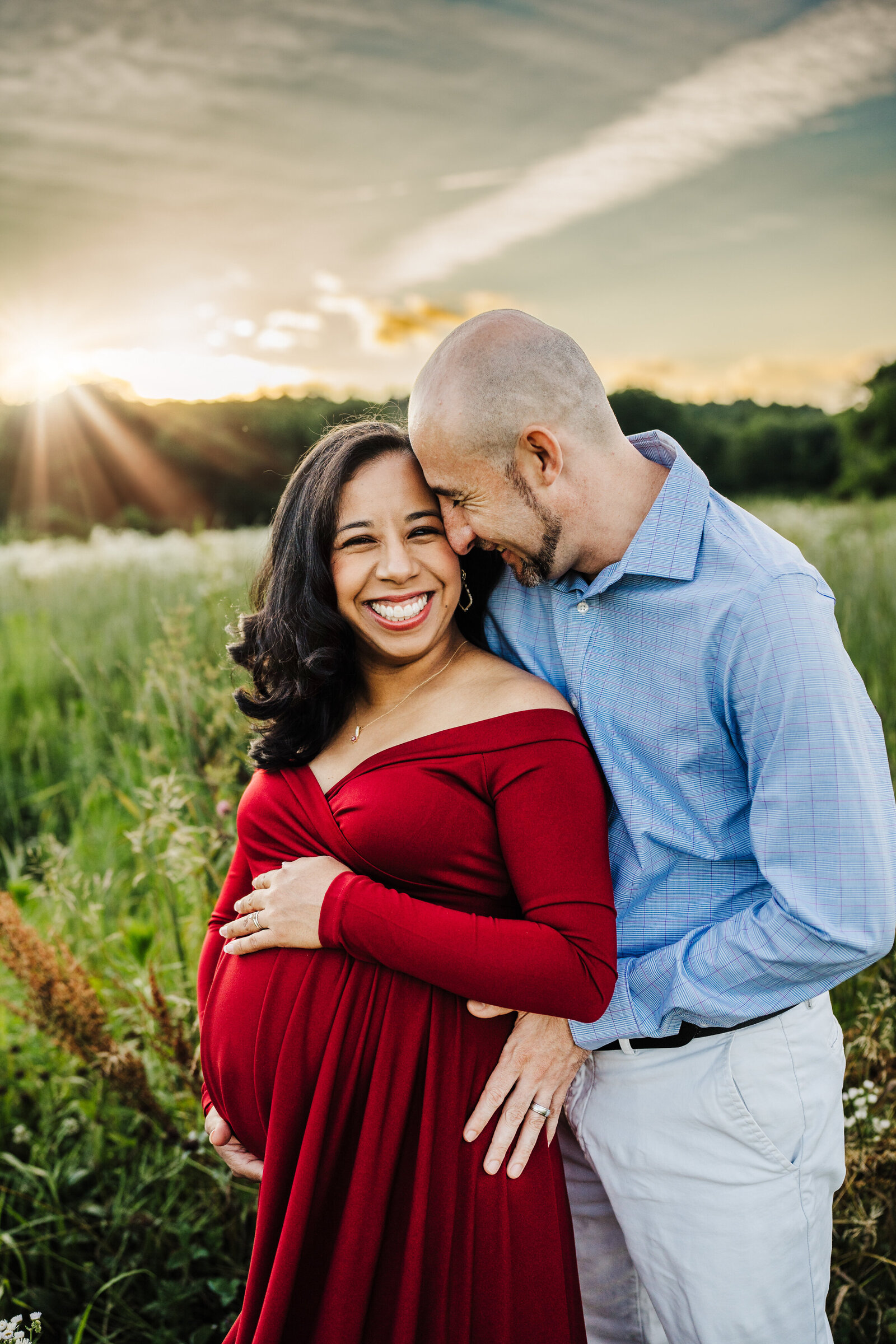 pregnant couple laughs together in field of flowers