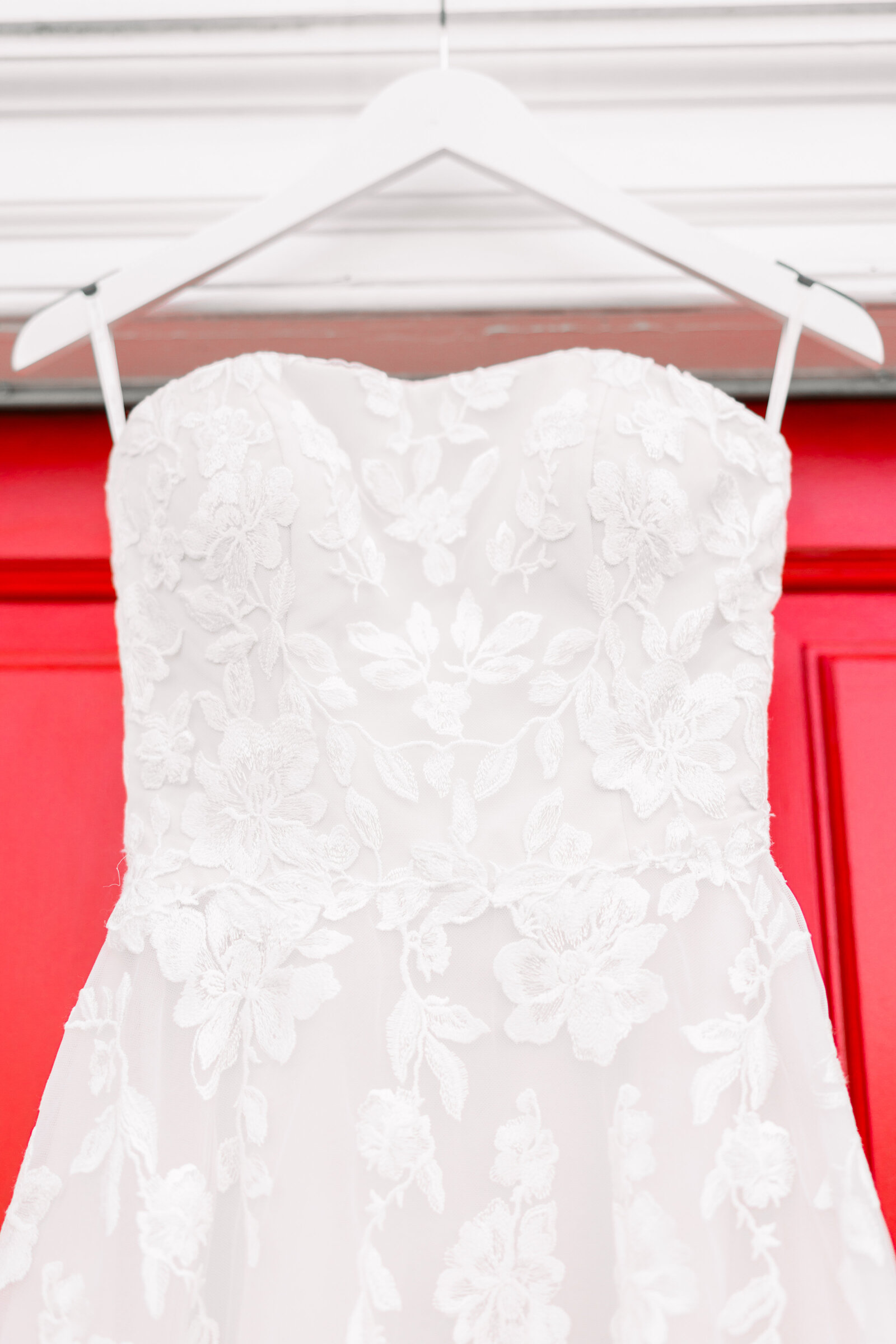 Wedding gown elegantly displayed against a striking red door at Inola in Blue Ridge, GA, showcasing classic bridal beauty and unique venue charm