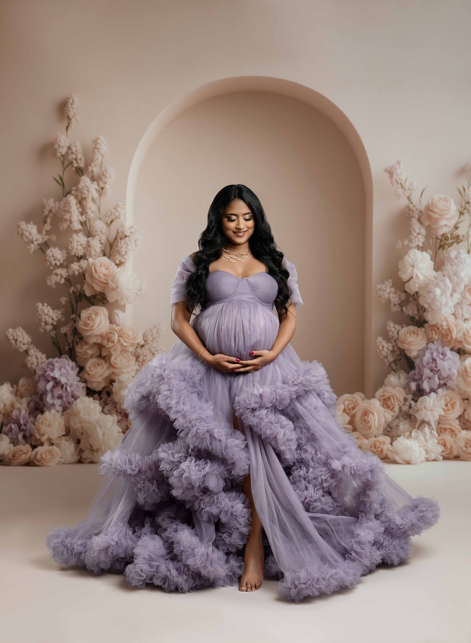 Pregnant women in lavender gown holding her baby bump and looking down.