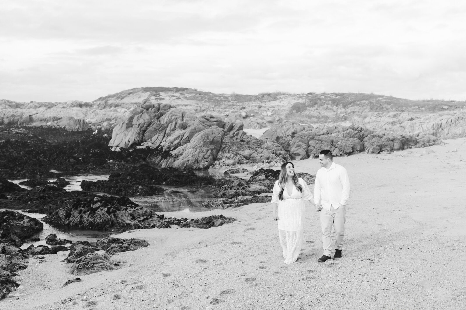 An engaged man and woman take photos on the beach in Pacific Grove, Monterey, California near Big Sur.