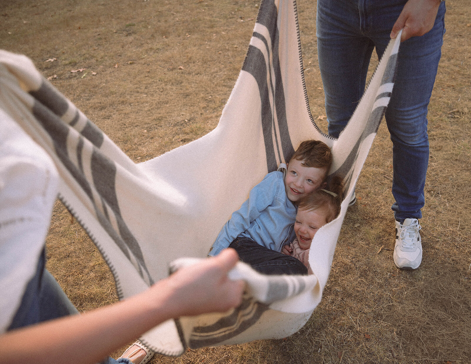 Two young kids laugh while being swung in a striped blanket during candid family photos near Irvine, CA.