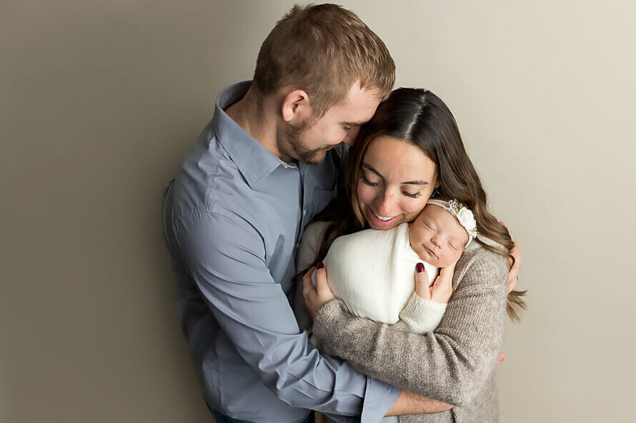 New parents hold their newborn baby in a photography studio.