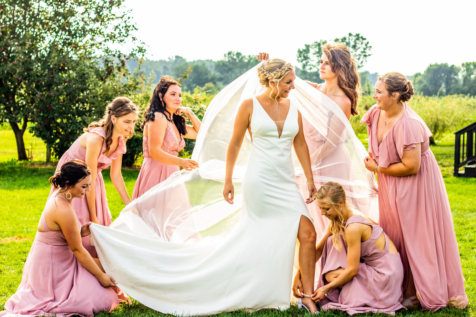 Bridesmaids in pink dresses fixing and fluffing the bride's dress. Photo by Devin Ramon Photography.